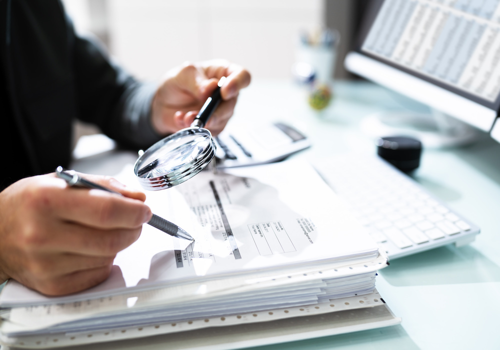 Audit And Fraud Investigation. Auditor Using Magnifying Glass On Document